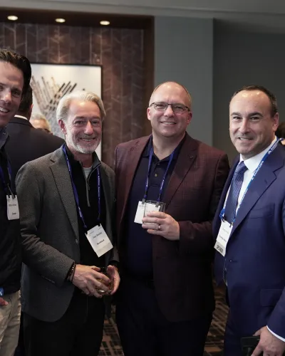 Four men in business attire smiling and posing together at a professional networking event indoors.