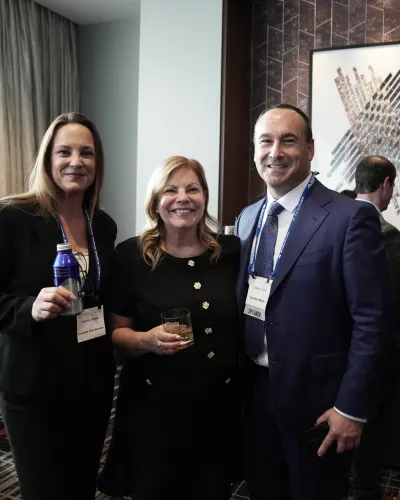 Three professionals smiling at a networking event with drinks in hand inside a modern conference room.
