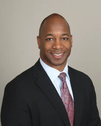 Smiling professional African American man in black suit and patterned tie against plain background
