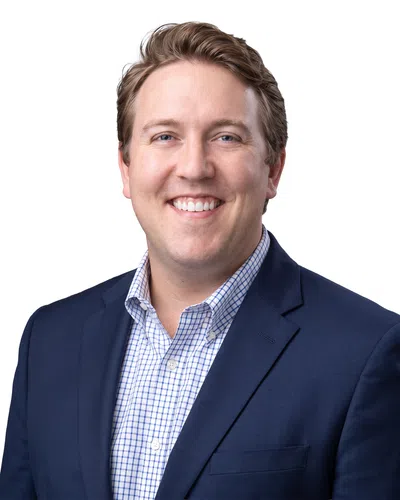 Smiling man in a blue suit jacket and checkered shirt against a white background