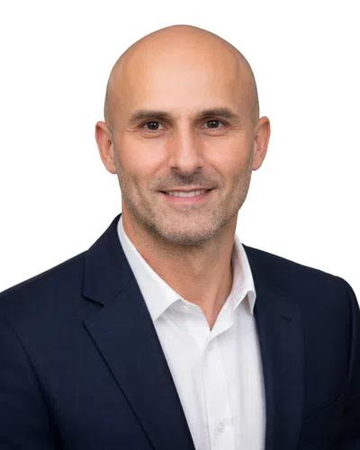 Smiling bald man in a dark suit jacket and white shirt on a white background.