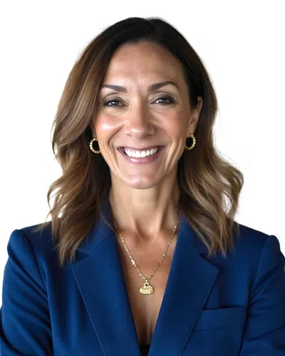 Smiling woman with wavy brown hair wearing a blue blazer, gold hoop earrings, and a pendant necklace.