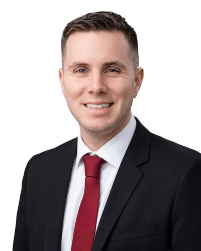 Smiling professional man in black suit, white shirt, and red tie with short brown hair against white background