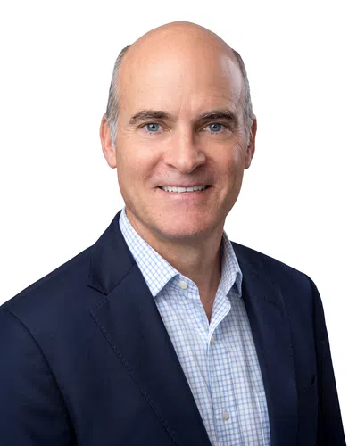 Smiling middle-aged man wearing a dark blazer and checkered shirt on a white background