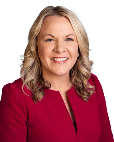 Smiling woman with blonde hair wearing a red textured top against white background, looking confident and approachable