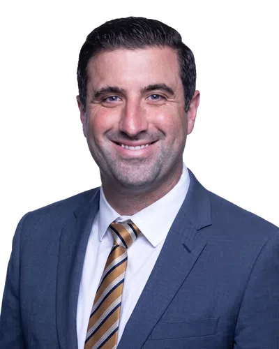 Smiling man in blue suit jacket, white shirt, and striped yellow and black tie against a white background.
