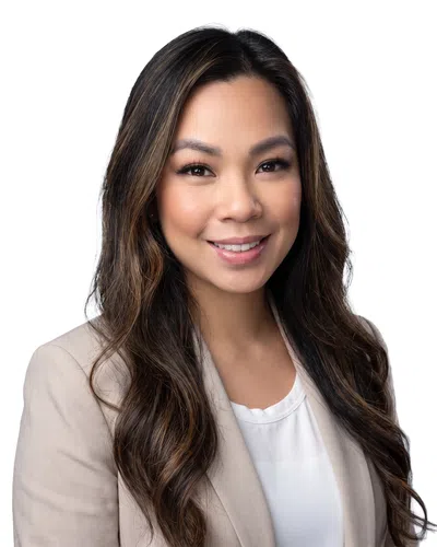 Smiling woman with long dark hair wearing a beige blazer and white top against a white background
