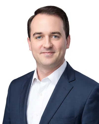 Portrait of a smiling man with blue eyes and dark hair wearing a suit and white shirt on a white background