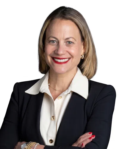 Professional woman in black blazer and white blouse smiling with arms crossed against white background.