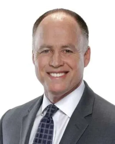 Smiling middle-aged man in a gray suit and patterned tie against a white background.