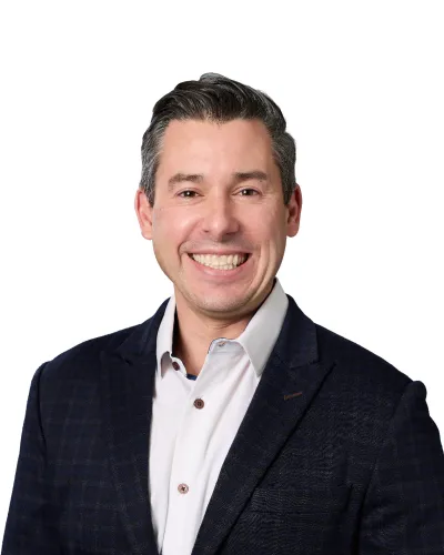 Close-up of a smiling man with short dark hair wearing a white shirt and dark textured jacket against white background
