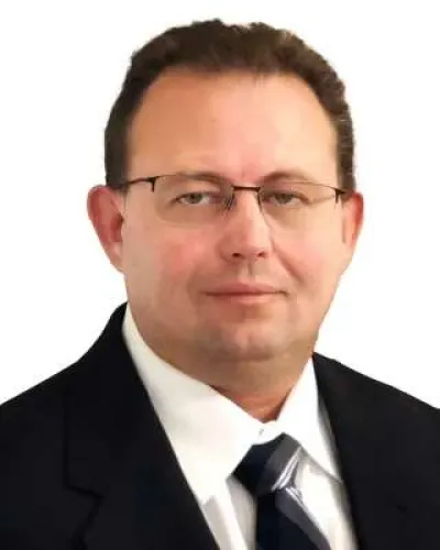 Professional man wearing glasses, suit, white shirt, and striped tie with neutral expression on white background