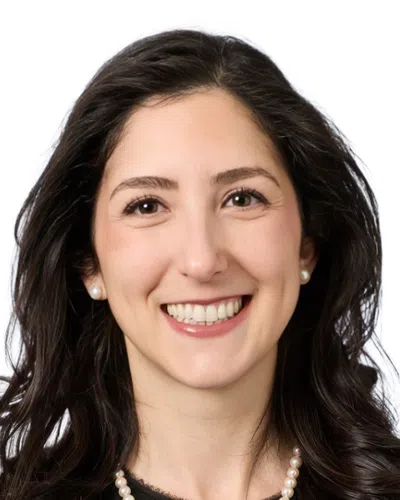 Smiling woman with short curly dark hair wearing a purple beaded necklace against a white background