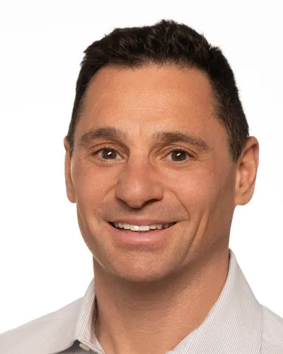 Smiling man with glasses wearing a navy suit and light blue shirt on white background
