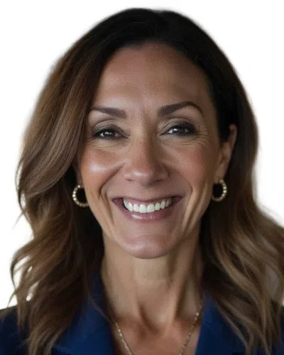 Confident businesswoman in blue blazer smiling with arms crossed in a modern office setting with blurred background.