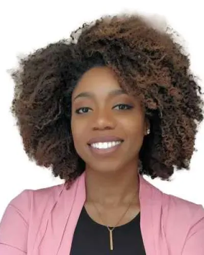Smiling woman with voluminous curly hair wearing a pink blazer and black top against white background