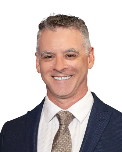 Smiling middle-aged man in navy suit and patterned beige tie against white background