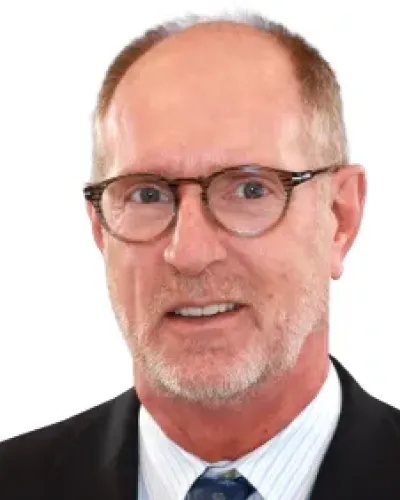 Middle-aged man with glasses wearing a suit, white shirt, and patterned blue tie, smiling slightly against white background.