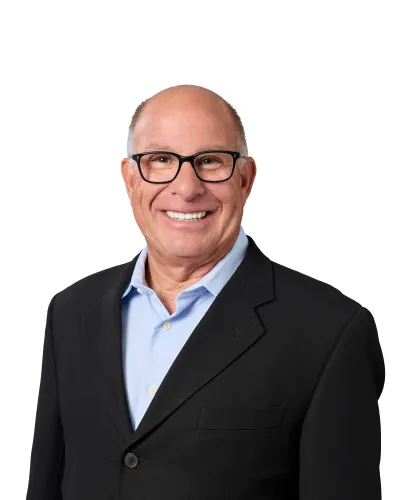 Smiling bald man wearing black glasses and a white shirt with a dark jacket against a white background