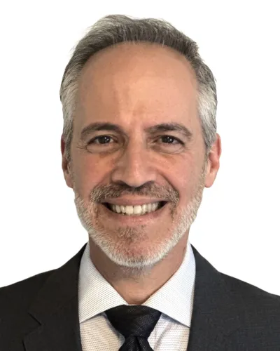 Smiling middle-aged man with gray hair and beard wearing dark suit, white shirt, and black tie against white background