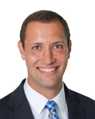 Smiling man in a dark suit with a white shirt and blue checkered tie against a white background