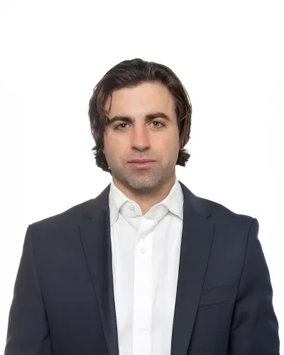 Professional man with medium-length brown hair wearing a navy suit jacket and white shirt against white background