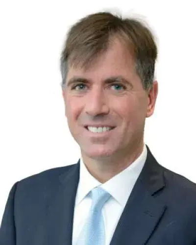 Professional man in blue suit with light blue tie smiling against white background