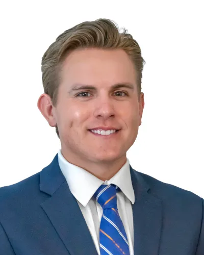Smiling young man with blond hair in a blue suit and striped blue tie on white background.