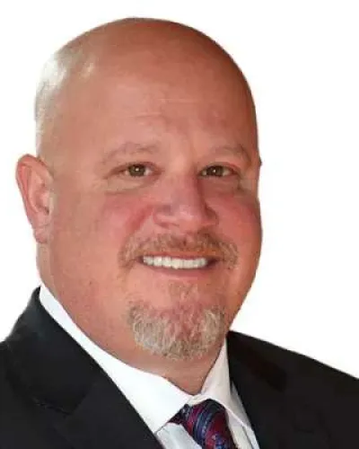Portrait of a bald man with a goatee, wearing a dark suit, white shirt, and striped tie, smiling