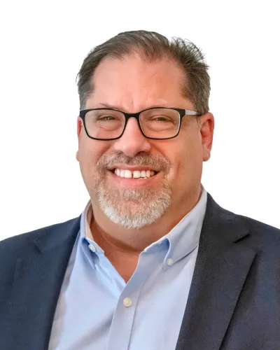 Middle-aged man with salt-and-pepper beard wearing a navy blue blazer and white shirt smiling at the camera