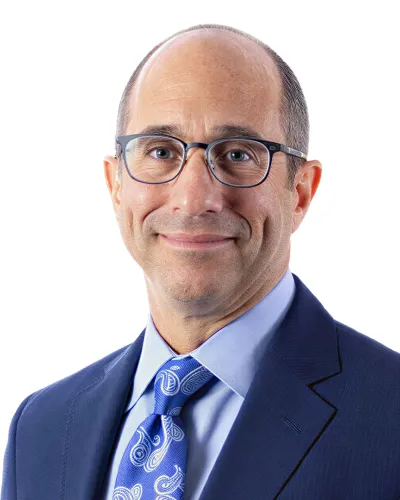 Professional middle-aged man with glasses wearing blue suit and patterned tie against white background