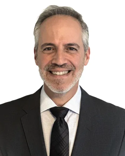 Smiling middle-aged man with gray hair and beard wearing dark suit, white shirt, and black tie against white background