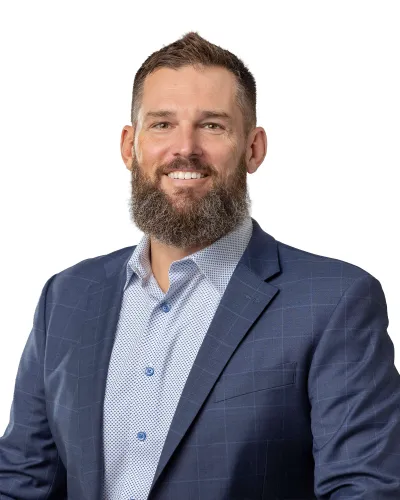 Smiling bearded man in a blue checkered blazer and patterned shirt on a white background