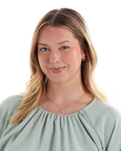 Young woman with blonde hair wearing a light green blouse and gold necklace against a white background