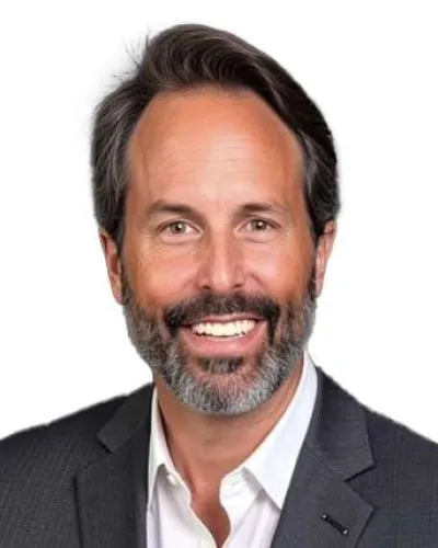 Smiling middle-aged man with salt and pepper beard wearing a dark suit and white shirt on white background