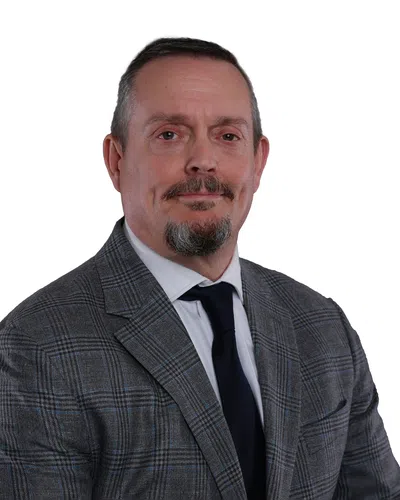 Middle-aged man with goatee wearing a gray plaid suit jacket and black tie on white background