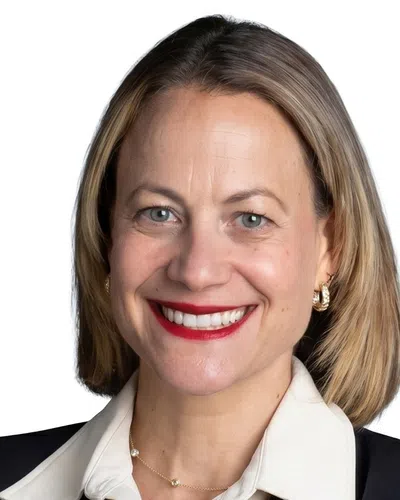 Professional woman in black blazer and white blouse smiling with arms crossed against white background.