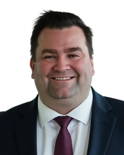 Smiling man in dark suit, white shirt, and maroon tie against a white background.