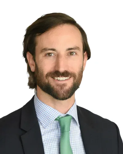 Smiling man with beard wearing a suit, checkered shirt, and green tie against white background