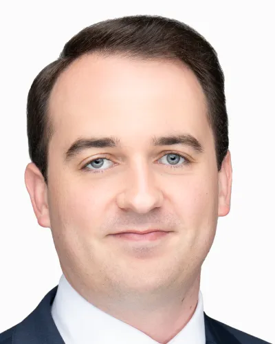 Portrait of a smiling man with blue eyes and dark hair wearing a suit and white shirt on a white background