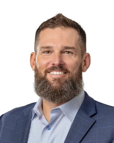 Smiling bearded man in a blue checkered blazer and patterned shirt on a white background