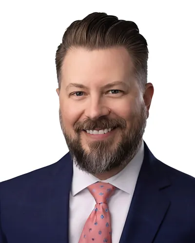 Smiling bearded man in navy suit and pink patterned tie with white background professional headshot.