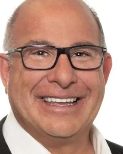 Smiling bald man wearing black glasses and a white shirt with a dark jacket against a white background