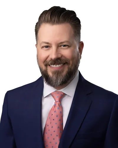 Smiling bearded man in navy suit and pink patterned tie with white background professional headshot.