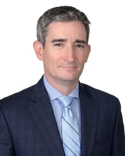 Professional middle-aged man wearing a dark suit and light blue striped tie against white background