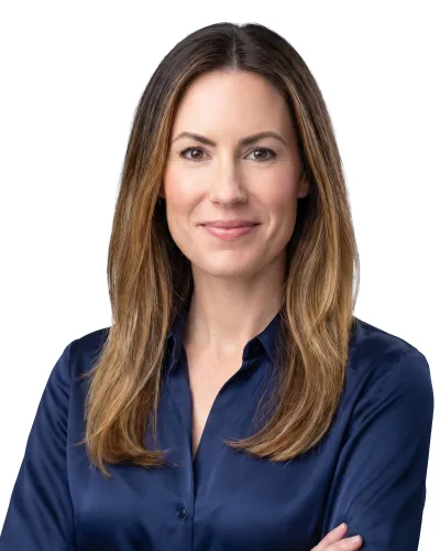 Smiling woman with long brown hair wearing a navy blue shirt against a white background