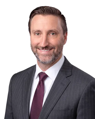 Smiling man in a dark pinstripe suit and maroon tie with neatly styled hair and beard on a gray background