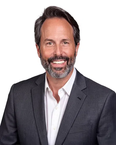 Smiling middle-aged man with salt and pepper beard wearing a dark suit and white shirt on white background