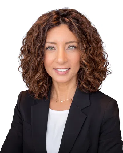 Confident businesswoman with curly hair wearing black blazer and white top smiling with arms crossed