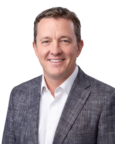 Smiling middle-aged man in gray plaid blazer and white shirt on a white background with no overlaid text.
